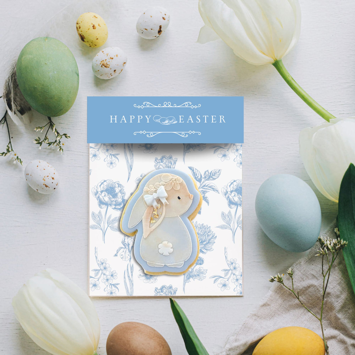 Blue Belle Easter backer card with a bunny cookie, styled with eggs and tulips